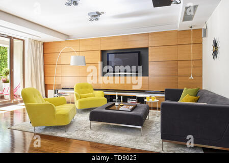 Built-in wall cabinets with TV next to sofa and two yellow armchairs in spacious living room    UK AND IRISH RIGHTS ONLY Stock Photo