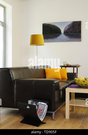 Yellow cushions on black leather sofa in modern sitting room   UK & IRISH USE ONLY Stock Photo