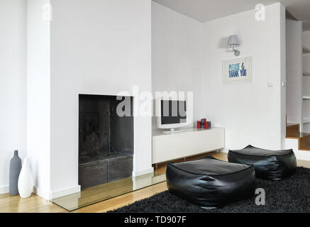 Two black leather poufs in front of TV next to open fireplace   UK & IRISH USE ONLY Stock Photo