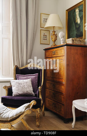 Gilt armchair and footstool in front of antique cabinet   UK & IRISH USE ONLY Stock Photo