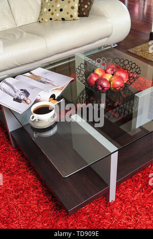 Cup of coffee and apples in wire fruit bowl on glass topped coffee table in front of cream leather sofa    UK AND IRISH RIGHTS ONLY Stock Photo