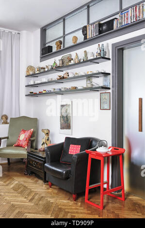 Collection of ceramic teacups and figurines on open shelves above armchairs and coffee table with drawer    UK AND IRISH RIGHTS ONLY Stock Photo