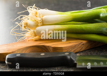 Green spring onions on wooden cutting board. Stock Photo