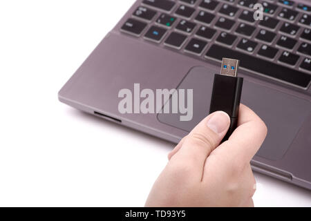 Young woman holding a black USB flash drive in her hand, with a defocused silver laptop with a keyboard in the background. Isolated on white backgroun Stock Photo