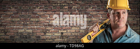 Male Contractor In Hard Hat Holding Level In Front Of Old Brick Wall Banner with Copy Space. Stock Photo