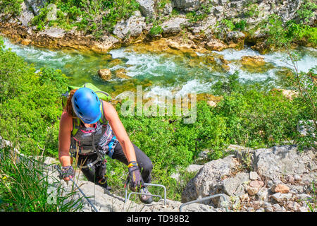 Via ferrata in Croatia, Cikola Canyon. Young woman climbing a medium difficulty klettersteig, with turquoise colors of Cikola river in the background. Stock Photo