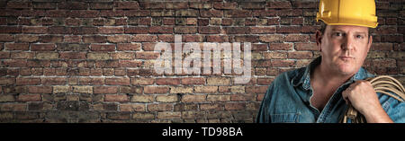 Male Contractor In Hard Hat Holding Cable In Front Of Old Brick Wall Banner with Copy Space. Stock Photo