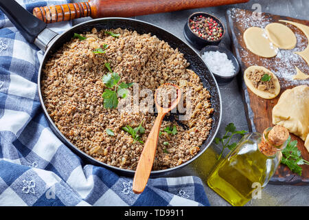 ground liver with onion fried in a skillet, ingredient of filling for pierogies, raw dough and uncooked dumpling on a cutting bord with rolling pin at Stock Photo