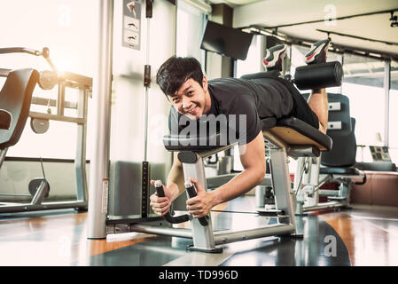 Asian sport man stretching and lifting weight by two legs when facing down for stretching muscle at fitness gym at condominium background. Sport and P Stock Photo