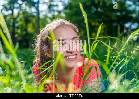 A young woman lies smiling in a meadow and looks to the side Stock Photo