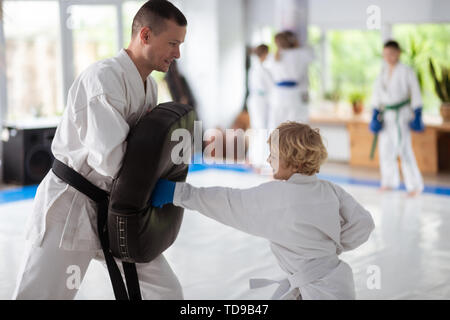 Improving strength. Curly blonde-haired boy loving martial arts improving his strength Stock Photo