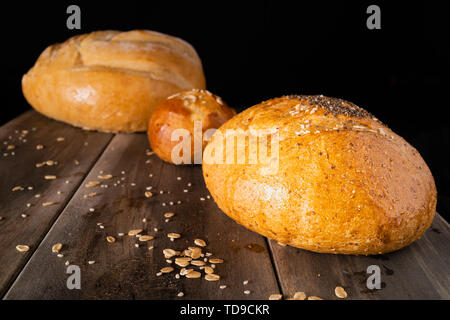 Three loaves of bread on an old wooden table with a dark background Stock Photo