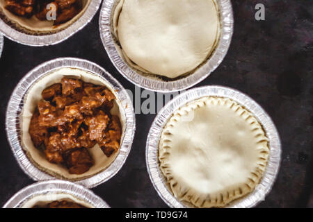 raw closed mini-quiche quiche stuffed with meat and mushrooms, on a dark background. view from above. Stock Photo