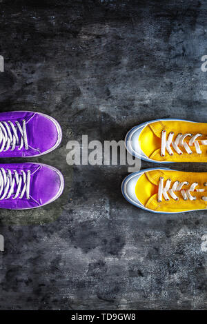 purple old worn dirty torn sneakers and and new yellow sneakers against a dark grunge background. view from above. Copy space. Stock Photo
