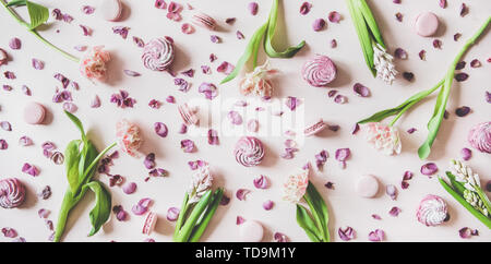 Flat-lay of macaron cookies, marshmallows and flowers over pink background Stock Photo