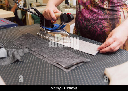 A woman strokes the fabric for further sewing. Tailor ironing clothes with industrial iron. Stock Photo