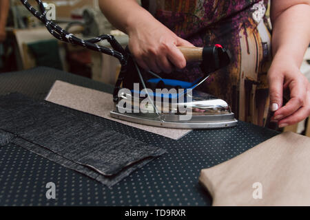 A woman strokes the fabric for further sewing. Tailor ironing clothes with industrial iron. Stock Photo