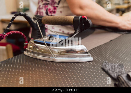 large, heavy, metallic iron in dry cleaning. woman ironing cloth for tailoring. production of clothes on an industrial scale Stock Photo