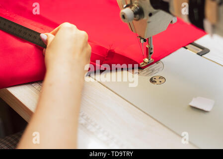 Tailor measures fabric with a ruler. Woman works in a garment factory. a tailor embroiders with a sewing machine on a crocheted fabric. Stock Photo