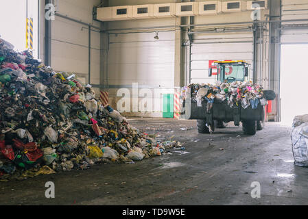 Tractor transports garbage at the plant for processing and sorting waste. Raised bulldozer bucket with waste. Pile of trash in the garbage factory Stock Photo