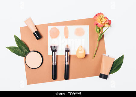 Samples of applying makeup foundation with different brushes and sponge blender on white background, flat lay. Stock Photo