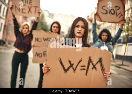 Women's march. Confident and young female protesting for equality and holding a signboard with word w=m while standing with other activists on the roa Stock Photo