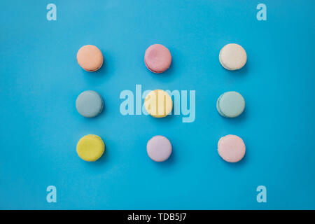 Multicolored cakes of almond flour with cream lie in three rows on a blue background. Macaroon top view. Stock Photo