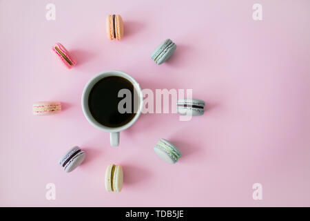 Multicolored macaroons lie around a cup of black coffee on a pink background. Flatlay. Watch concept. Stock Photo