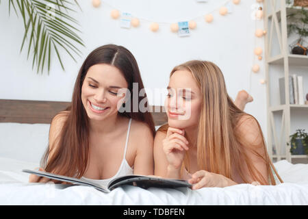 Friends together at home lying on bed reading magazine curious smiling Stock Photo