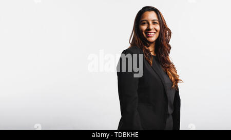 Side view of smiling businesswoman standing against white background looking at camera. Portrait of smiling businesswoman in formal suit having golden Stock Photo