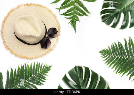 Straw beach sun hat with sunglasses,border of tropical monstera and fern on white. Top view with copy space. Summer concept. Tropical vacation. Stock Photo