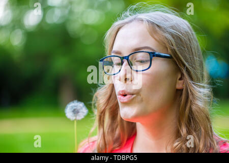A young woman holds an dandelion in her hand and blows Stock Photo
