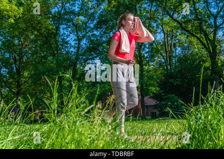 A young woman in running training wipes the sweat with a towel from her face Stock Photo