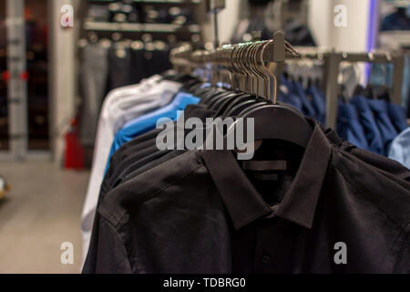 Trade, interior and shopping concept - black, blue and white men's shirts on hangers inside the store, close-up with a blurred background Stock Photo