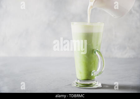 Green matcha tea and pouring milk in latte glass on grey table. Space for text. Close up. Horizontal orientation. Stock Photo