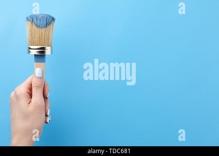 Female hand holding brush tool in paint on blue background, copy space Stock Photo