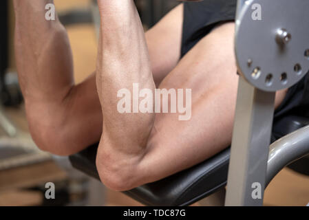 Man flexing isquiotiobial leg muscles on leg curl gym machine. Sport, fitness, bodybuilding and people concept . Stock Photo