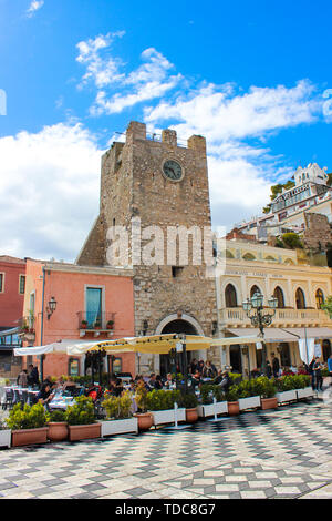 Taormina, Sicily, Italy - Apr 8th 2019: Tourists sitting in outdoor restaurants and cafe on Piazza IX Aprile square in front famous Clock Tower. Stock Photo