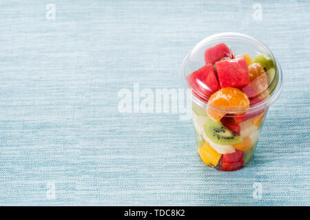 Fresh cut fruit in a plastic cup on blue background Stock Photo