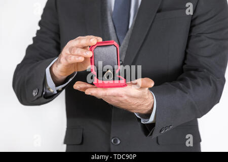 Man in a black suit gives a ring with a diamond in a red box Stock Photo