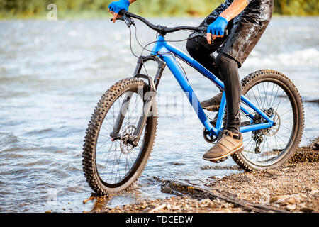Professional well-equipped cyclist riding on the rocky riverside in the mountains. Close-up with no face Stock Photo
