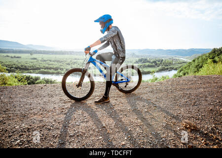Professional well-equipped cyclist riding bicycle on the rocky mountains with beautiful landscape view during the sunset Stock Photo