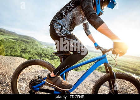 Professional well-equipped cyclist riding bicycle on the rocky mountains with beautiful landscape view during the sunset Stock Photo
