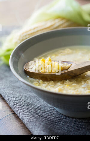 Corn egg soup corn soup in a ceramic bowl with a wooden spoon with a corn grain background is gray cloth and corn. Stock Photo