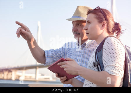 Senior man in summer hat shows the way on the map to young woman. Stock Photo