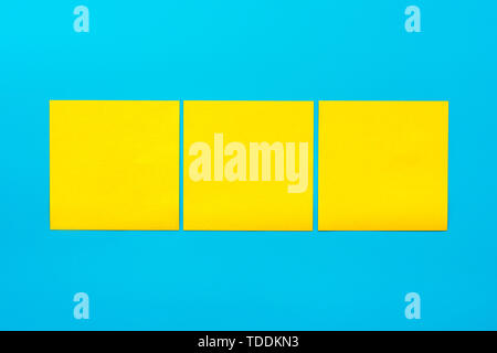 Reminder and combination concept- Close up three yellow empty square stickers on blue background with copy spase, mock up horizontal orientation. Stock Photo