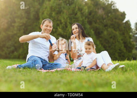 Happy family has fun playing with soap bubbles on the grass in the park. Stock Photo