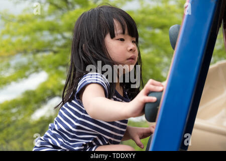 Cute little girl is climbing up on ladder in playground Stock Photo