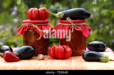 Eggplants in tomatoes in jars are located on a table in the garden, Fresh tomatoes, aubergines, garlic and bell peppers are on the table, blanks for t Stock Photo