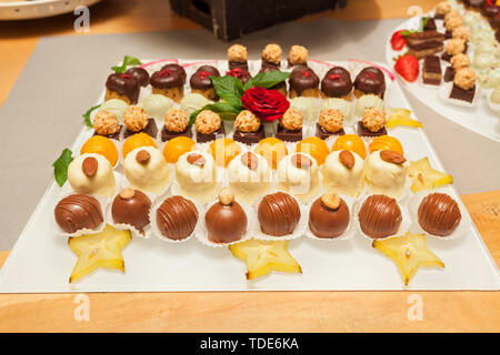 Small assorted cakes lined up decorated on dessert buffet with red rose and mint leaves, with slices of Carambola fruit Stock Photo